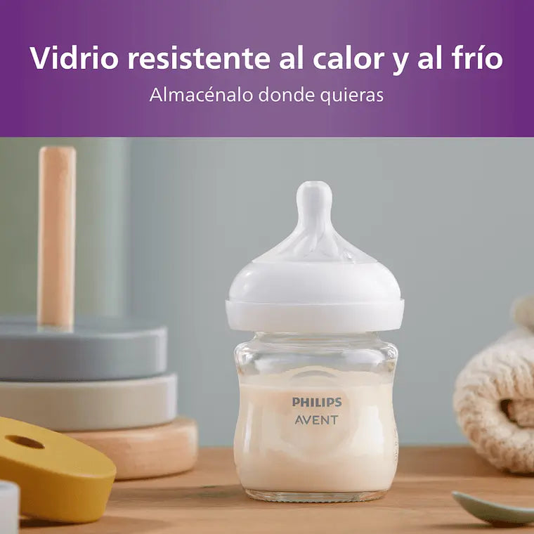 Mamadera Philips Avent Natural Response 120ml Vidrio con leche a un costado de juguetes con fondo gris